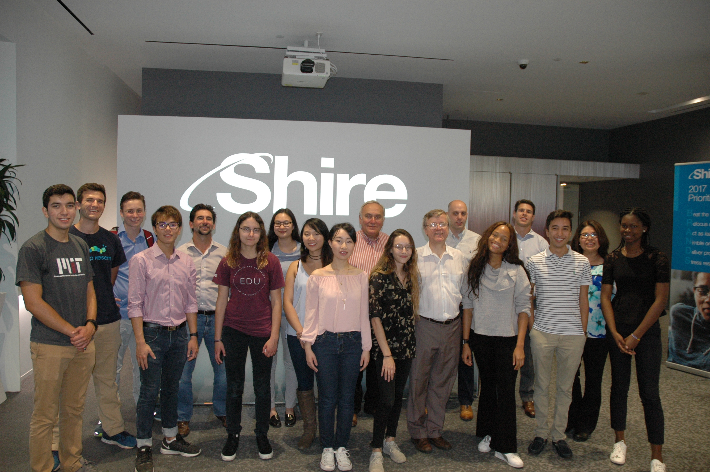 Students from the 10.28 class and speakers from Shire stand in front of the Shire logo.