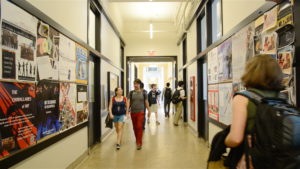 Students walk down the Infinite Corridor. The walls are covered in posters for events and activities.