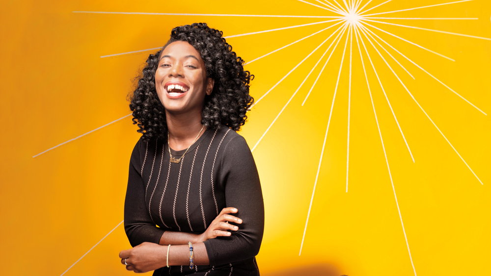 Janelle Heslop laughing in front of a bright yellow background