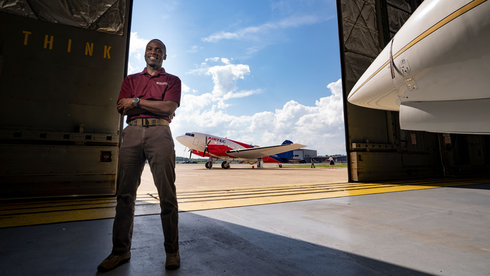 MIT alumnus Thomas Washington standing in an airplane hanger with planes behind him