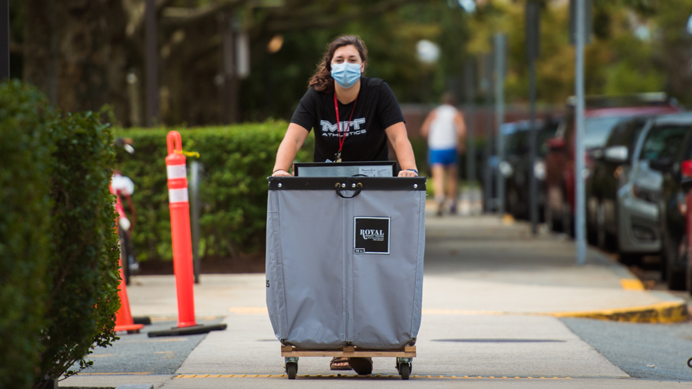 An incoming MIT student pushes a wheeled bin along a sidewalk at MIT