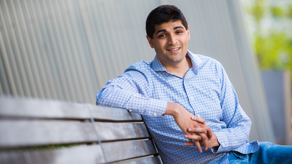 Ankur Moitra sitting outside on a bench on the MIT campus