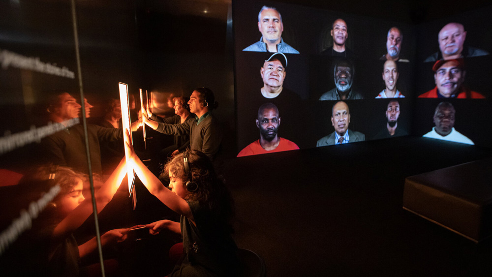 child and adults touching a glowing screen, with faces projected on the walls