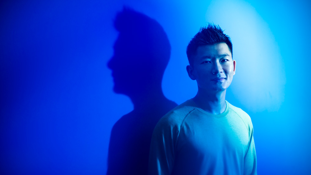 Heng Yang standing against a wall and bathed in blue light