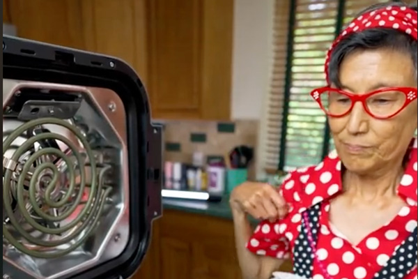 Lynn Yamada Davis dressed in red and white polka dots looking at a small cooking burner