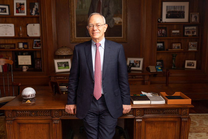 Photo of President Rafael Reif in his office with wooden desk and shelves in background.