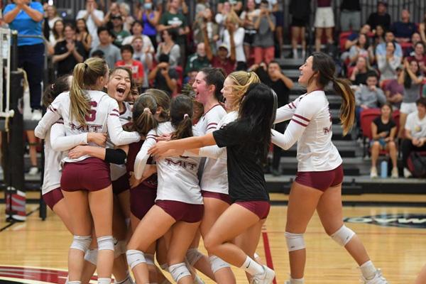 The MIT Women's Volleyball Team hugging each other and smiling on an indoor volleyball court 