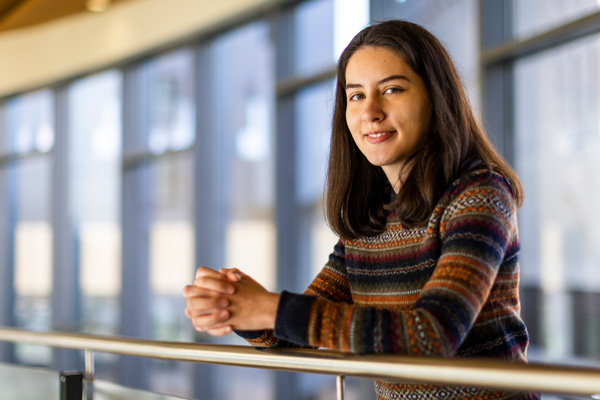 Valeria Robayo leans against a railing with MIT Sloan windows in background.