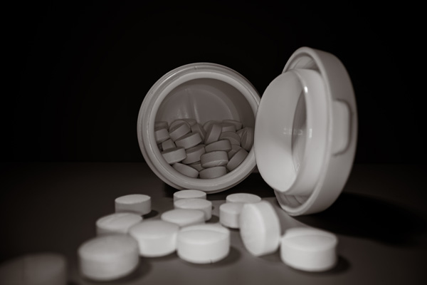 White pills in an open container on black background