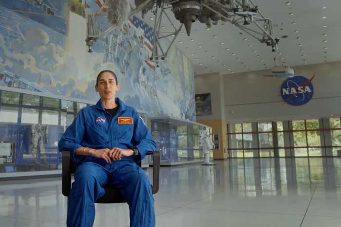 Jasmin Moghbeli sits in a chair in a large room with NASA memorabilia and murals, and a NASA logo in background