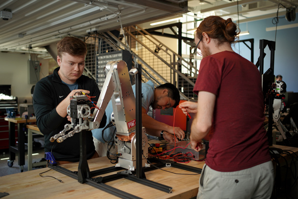 Andrew SaLoutos, Hongmin Kim, and Elijah-Stanger-Jones working on a robot arm in a lab