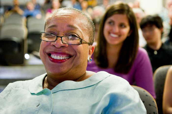 In foreground, Blanche Staton smiles while seated in an audience, with smiling people in background