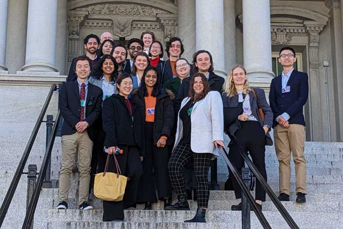 About 18 people pose for a photo on the steps of a building