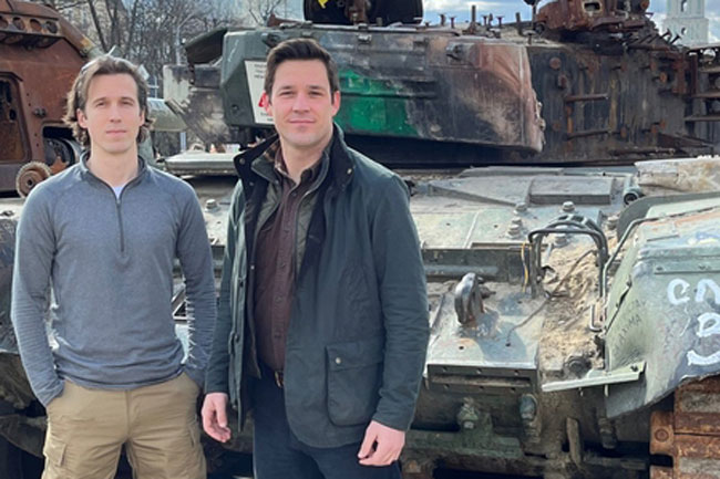 Ian Miller and Evan Platt stand in front of a battered tank