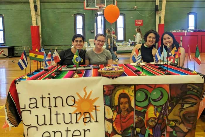 4 people sit at the decorated Latino Cultural Center organization table inside a gym