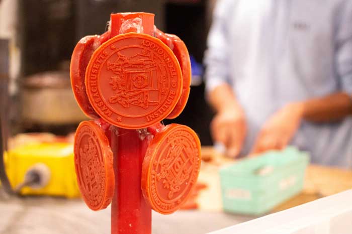 Some orange wax medallions are drying after being removed from a mold. They are together on a rod, with shop in background