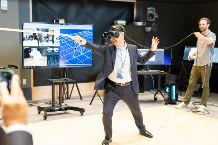 A man in business suit in a fencing stance as he wears Augmented Reality goggles. A screen showing data is in the background