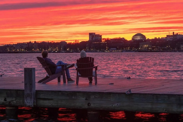 two people sitting on a dock watching a colorful sunset over MIT's campus