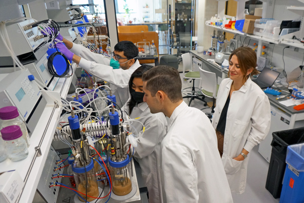 four people wearing white lab coats working in a lab