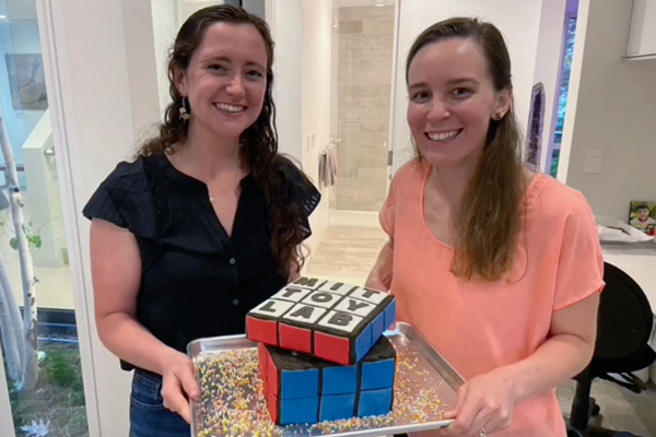 Charlotte Folinus and Georgia Van de Zande holding a Rubik's Cube cake