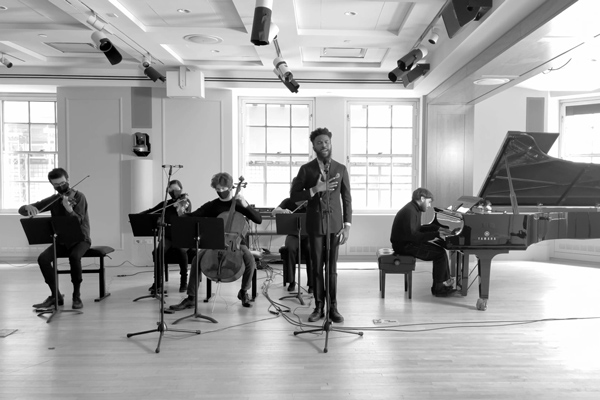 Joshua Bennett reciting at a microphone backed by five musicians