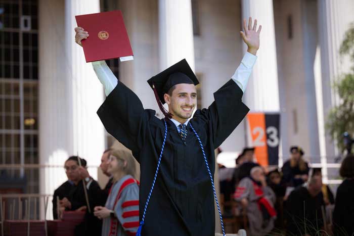 Graduate raises arms in triumph as he walks away with his diploma
