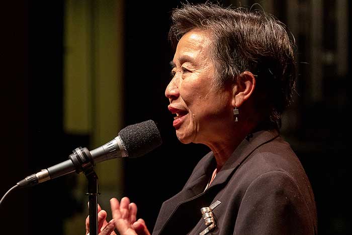 Photo by Mike Nyman via The Moth. Sawyer, seen in profile, speaks on stage into a microphone.