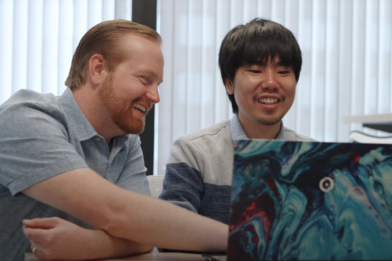 Glen Junor and a student smile as they collaborate together and look a laptop screen.