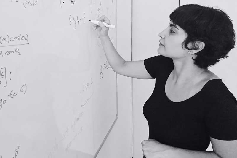 Leila Mirzagholi writes math equations a white board