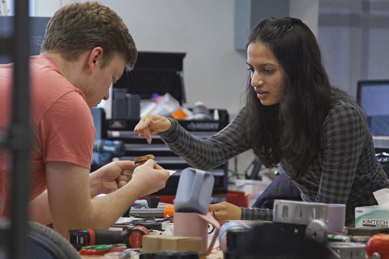 A person, left, and Sharmi Shah, right, hunch over a cluttered table, examining some small object