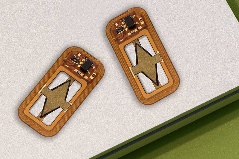 Two tiny rectangular devices have curved edges. The devices are orange-yellow and are made of a circuit board and soldered pieces, including a diamond-shaped piece of material in the middle.