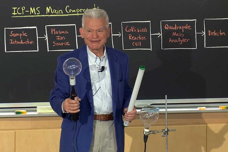 John Dolhun teaches, holding 2 lights, in front of a blackboard.