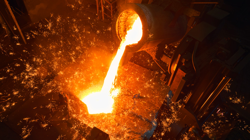 Glowing molten metal is poured in a dark factory, with lots of orange sparks