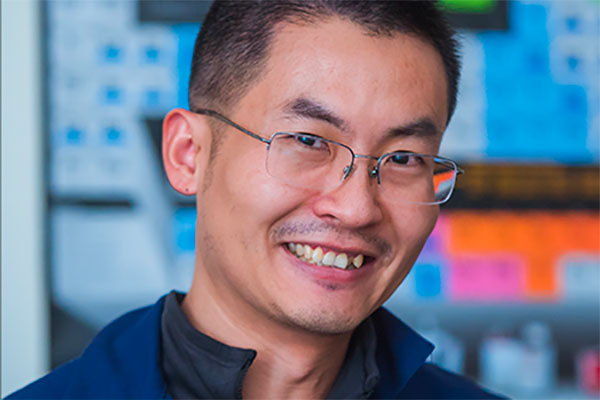 Headshot of Mingda Li, male faculty member in a lab setting with instuments in the background, MIT