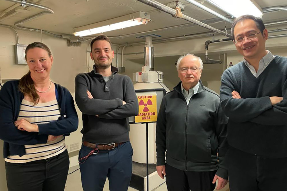 Jennifer Rupp, Thomas Defferriere, Harry Tuller, and Ju Li pose standing in a lab, with a nuclear radiation warning sign in the background