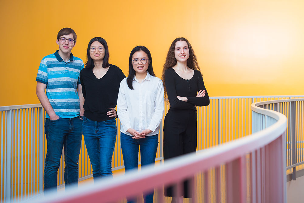 Four students on a curved walkway indoors against an orange backdrop, MIT