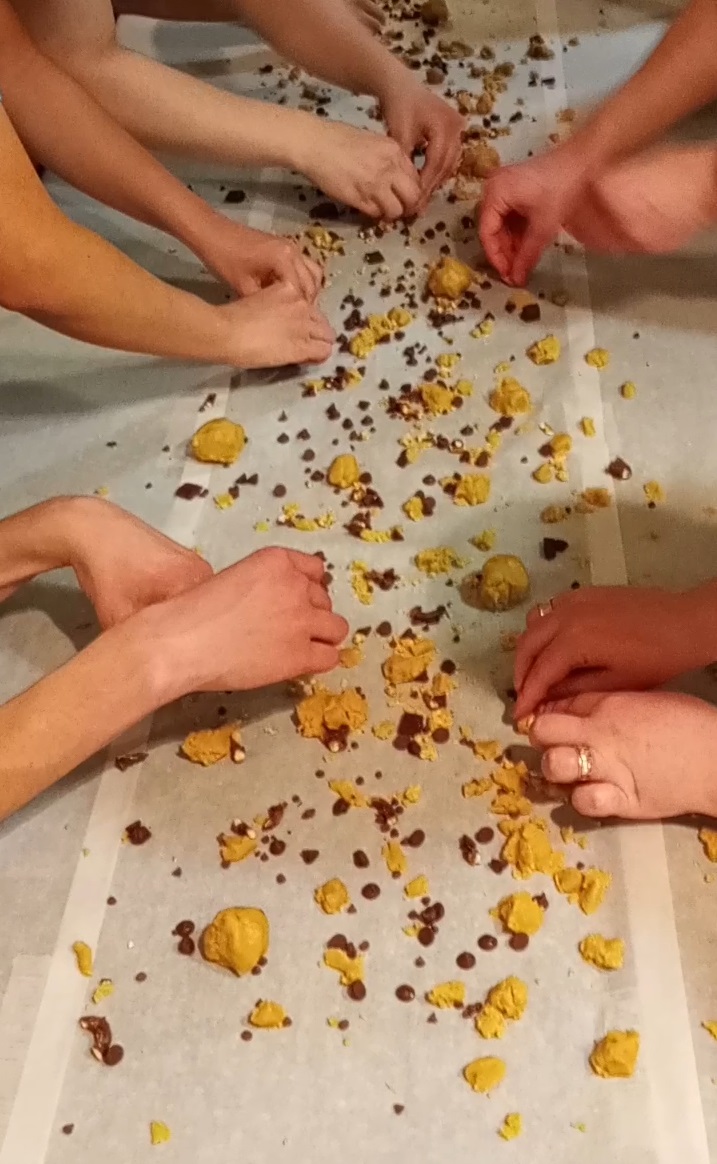 A group of people rolling balls of cookie dough on a table full of cookie dough fragments in the style of Katamari Damacy or Agar.io
