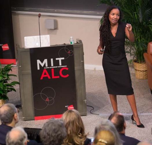 A presenter stands next to a lectern that says MIT ALC.