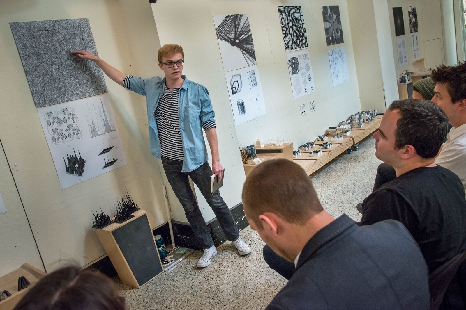 A student stands and points at a printout on the wall while several people in seats look on.