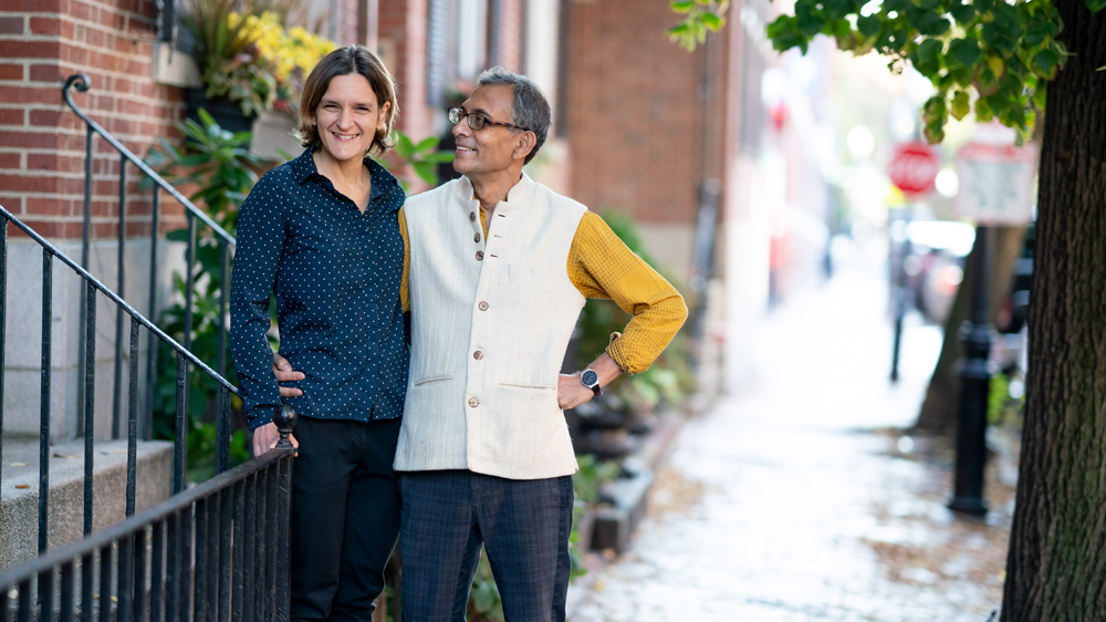 Esther Duflo and Abhijit Banerjee stand on the steps of their brick home