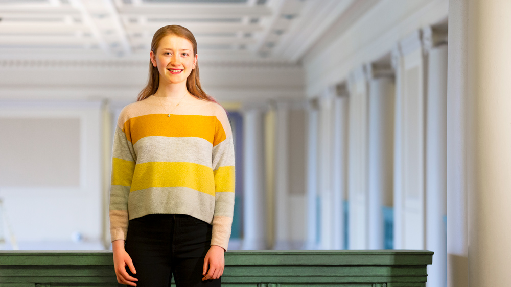 Emily Soice standing in front of a green railing with Lobby 7 columns behind her