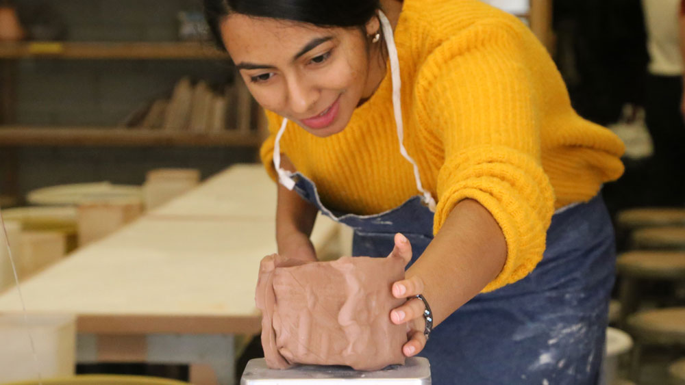 A female student weighing a blob of clay on a scale