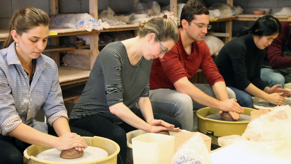 Students sitting next to each other working with clay on pottery wheels