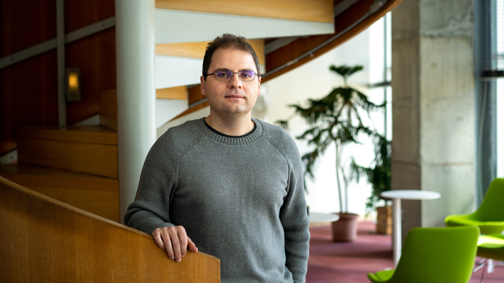 Aleksander Madry wearing glasses and a gray sweater while standing on a spiral staircase
