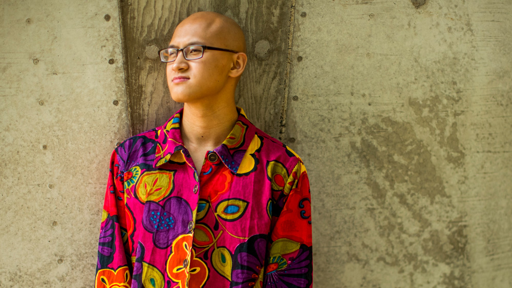 Kevin Lee in a colorful shirt standing in front of tan wall