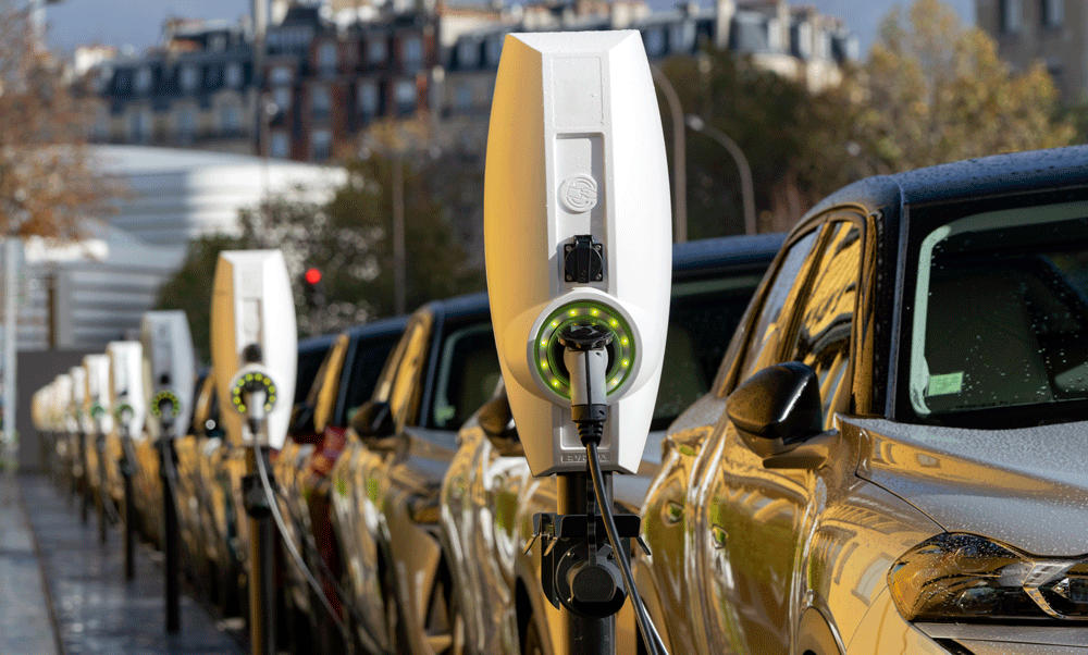 a line of electric cars on a city street connected to chargers