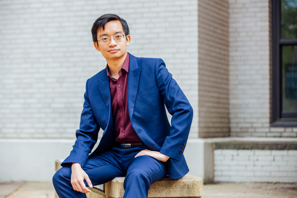 Minh Trinh sitting in front of a white brick building