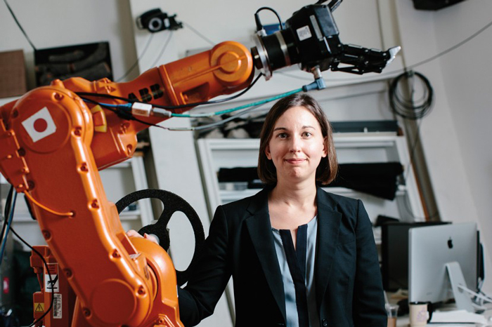 Photo of Julie Shah next to large orange robot hand, by M. Scott Brauer, courtesy of Spectrum