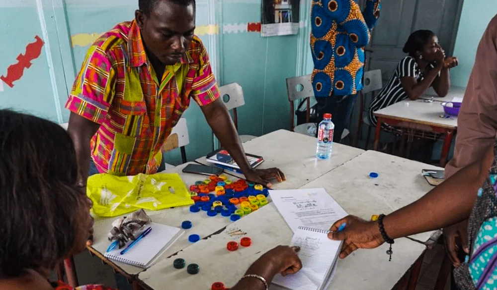 Three teachers in Ghana in conversation standing around a table of colorful teaching materials