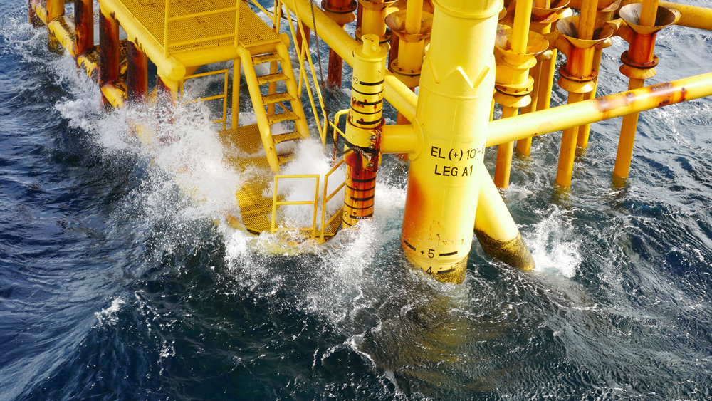 A photo shows waves hitting a yellow oil rig-style structure